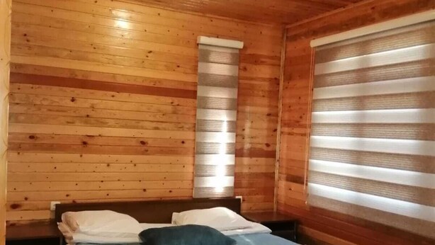 Une pièce de cabane en bois comprenant un lit, des oreillers et une fenêtre avec des stores.