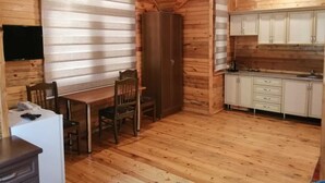 L’intérieur d’un chalet en bois comprend un coin repas, une cuisine et un téléviseur fixé au mur.