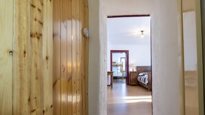 Um corredor de madeira que dá para um quarto com uma cama, uma mesa de cabeceira e um abajur.