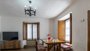 Uma sala de jantar espaçosa com mesa e cadeiras de madeira, uma televisão em um aparador de madeira e um lustre.
