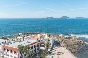 Un hôtel situé sur la côte, offrant une vue sur la mer, les palmiers et un paysage rocheux.