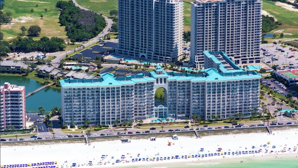 Un hotel de gran altura con varios balcones, vista a la playa y zona de estacionamiento.