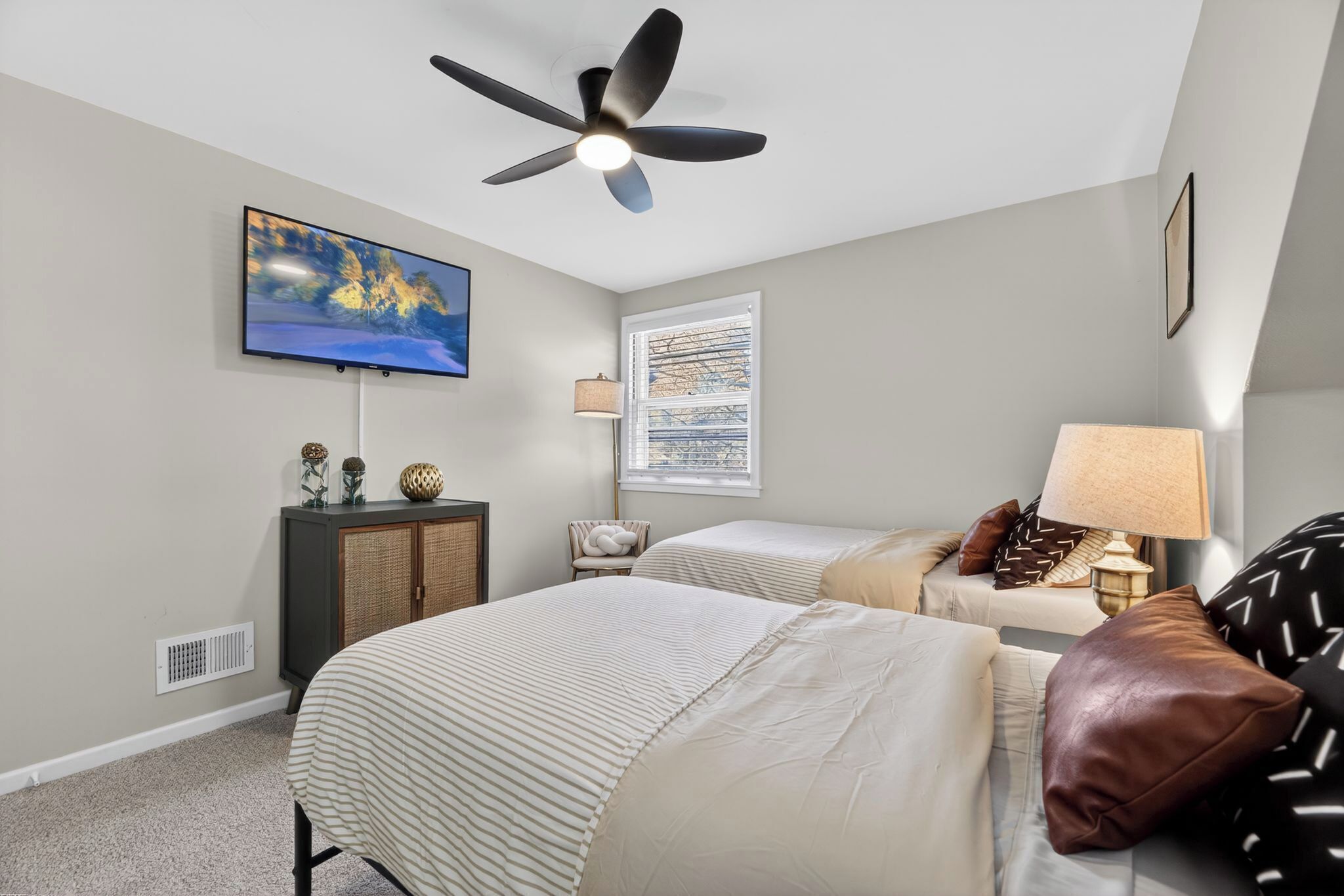A bedroom with two beds, a ceiling fan, a TV, a window with blinds, and a lamp.