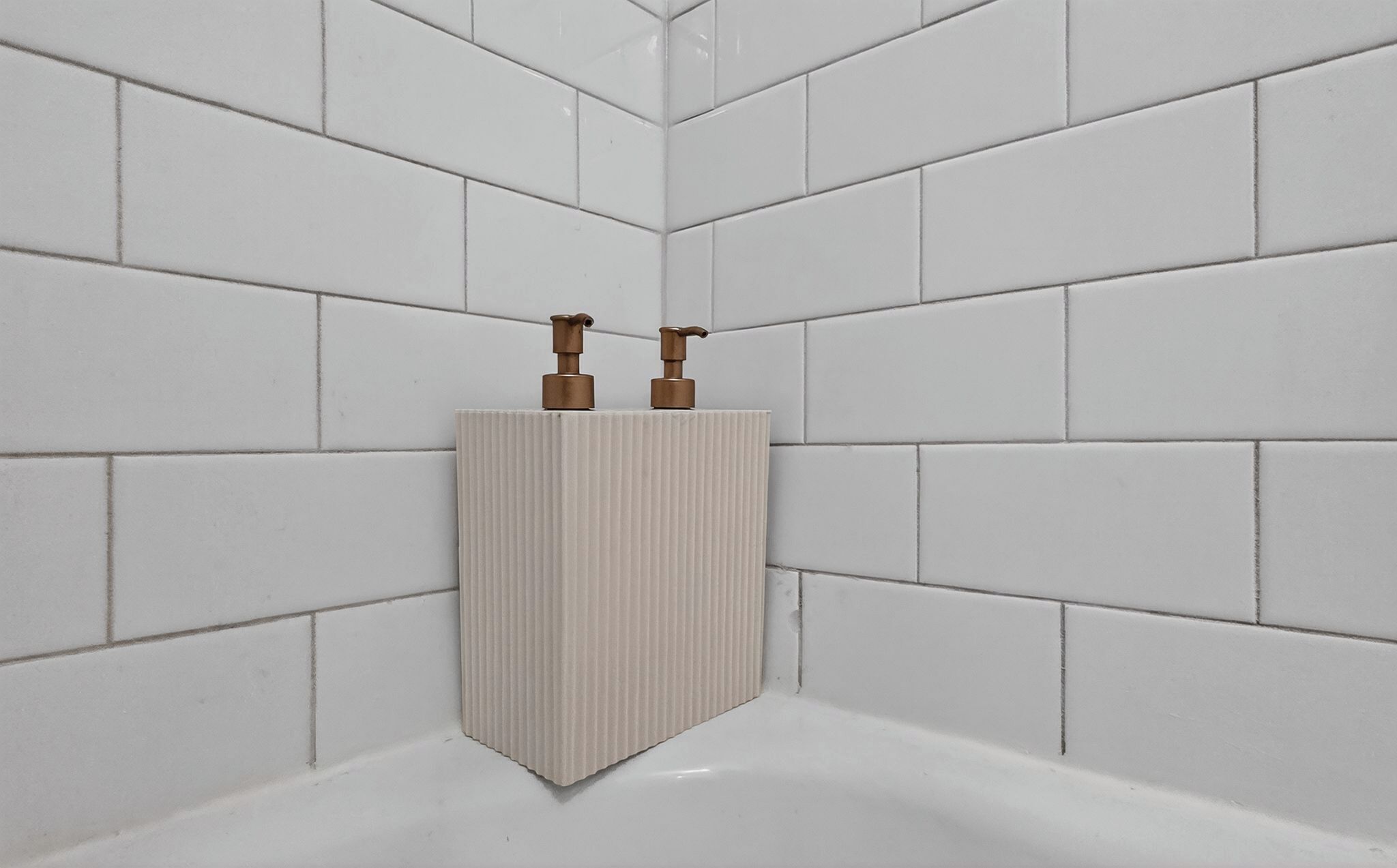 Une salle de bain avec des murs recouverts de carreaux blancs et un lavabo blanc doté de deux robinets en bronze.