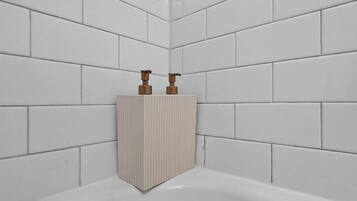 Une salle de bain avec des murs recouverts de carreaux blancs et un lavabo blanc doté de deux robinets en bronze.