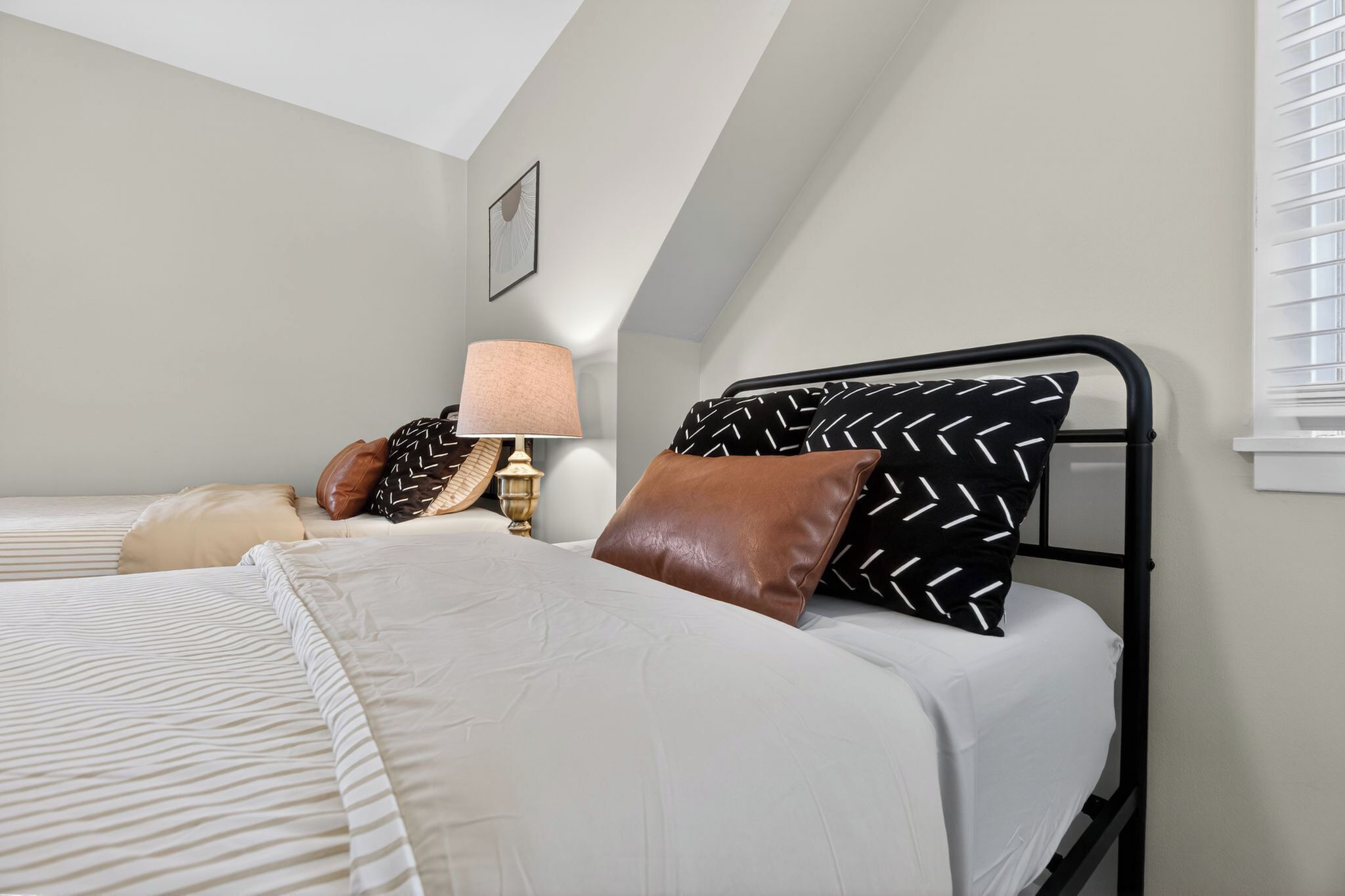 Een slaapkamer met een bed, kussens, een lamp en een foto aan de muur.