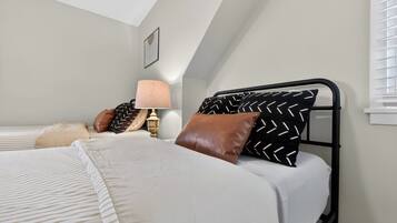 Een slaapkamer met een bed, kussens, een lamp en een foto aan de muur.