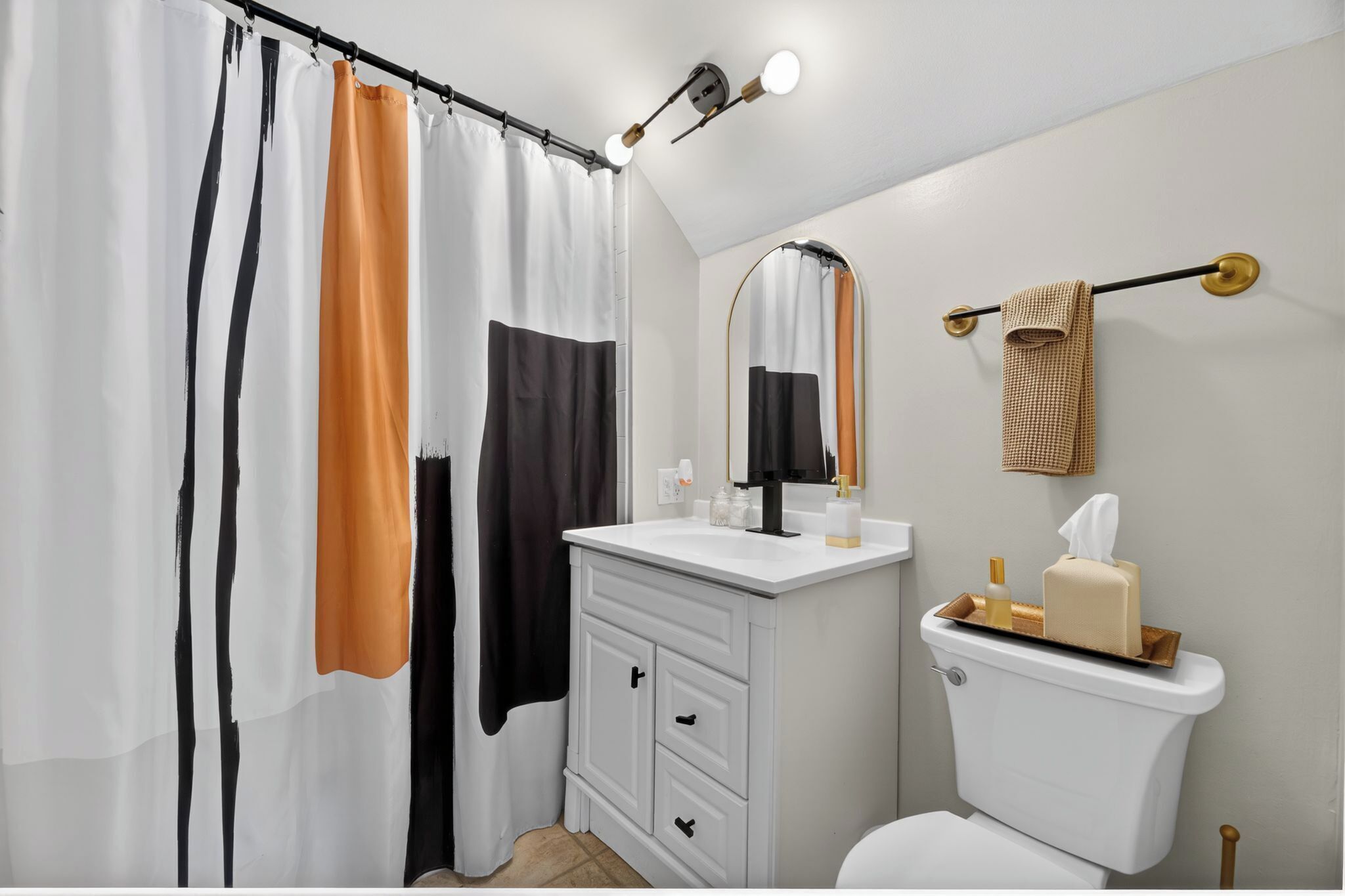 Une salle de bain avec un rideau de douche, des toilettes, un lavabo avec un miroir et un porte-serviettes.