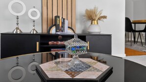 Un interior moderno con una mesa de vidrio, un mueble negro con libros y objetos decorativos.
