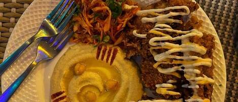 A plate with a fried dish, a side of coleslaw, and a dollop of sauce on a woven table mat.