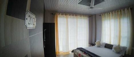 A hotel room with a large bed, a ceiling fan, and a sign indicating room number 202.