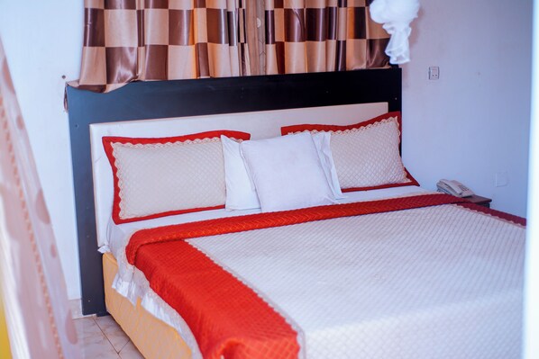 Un lit bien fait, recouvert d’une couvre-lit rouge et blanche, avec une tête de lit en bois et un téléphone posé sur la table de chevet.