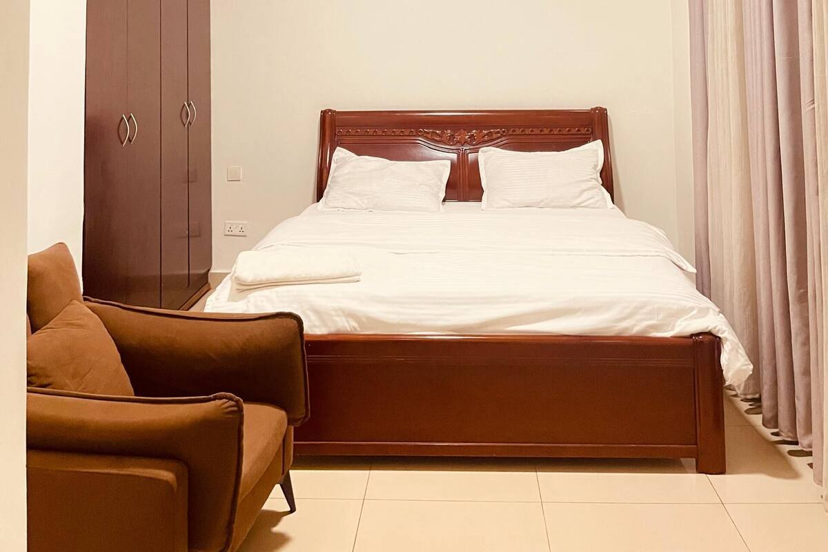 Un dormitorio con una cama de madera, un armario marrón y un sillón marrón.