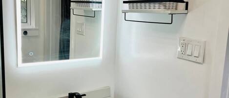 A bathroom with a white vanity, a mirror, a black faucet, and two white cabinets. There are two white wicker baskets on floating shelves above the vanity.