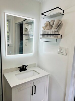 A bathroom with a white vanity, a mirror, a black faucet, and two white cabinets. There are two white wicker baskets on floating shelves above the vanity. - Walk to Midtown - Fire, Bikes, Capitol 1M, FSU 2M (Tallahassee)