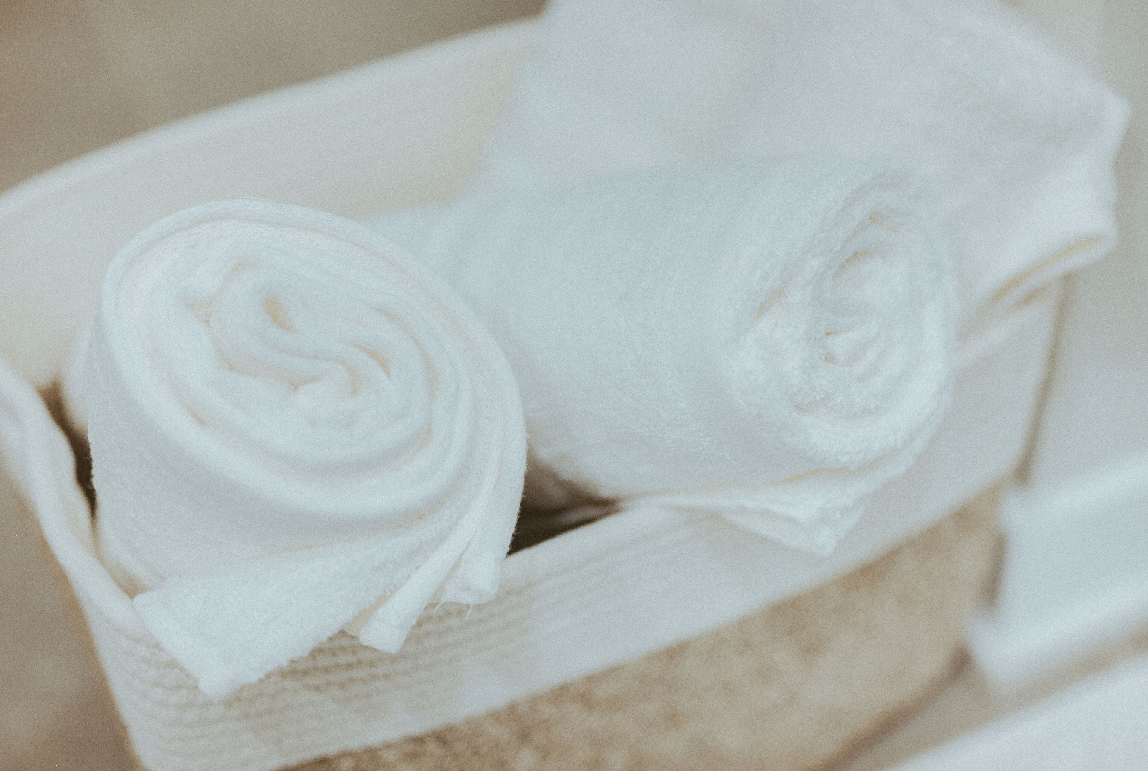 Um item de tecido branco e texturizado, possivelmente uma toalha ou pano, enrolado e colocado dentro de um recipiente bege e texturizado.