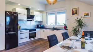 A modern kitchen with a black refrigerator, white cabinets, and a dining area with a table set for two. - 6 bedroom amazing home in Bilice (Bilice)