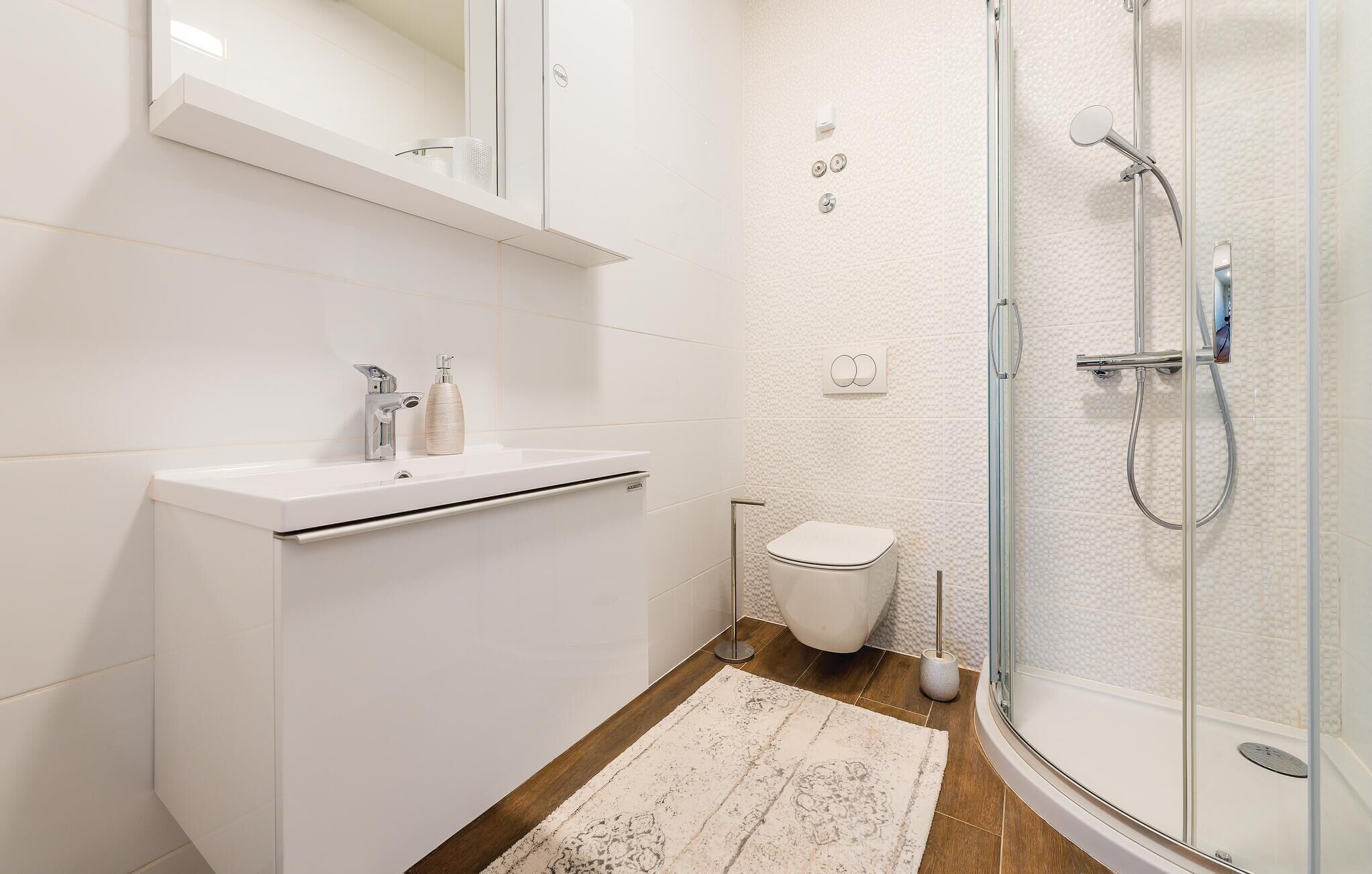 A modern bathroom with a glass-enclosed shower, a white sink with a soap dispenser, and a toilet.