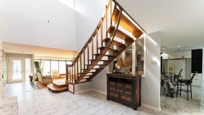 Een ruime woonkamer met een houten trap, marmeren vloer en een eetgedeelte met moderne meubels.