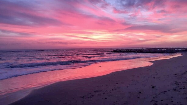 Ein Strand mit Sonnenuntergang, Wellen und einer entfernten Küste.