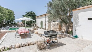 Eine Terrasse mit Pool, Gartenmöbeln, Grill und einer Steinsäule.