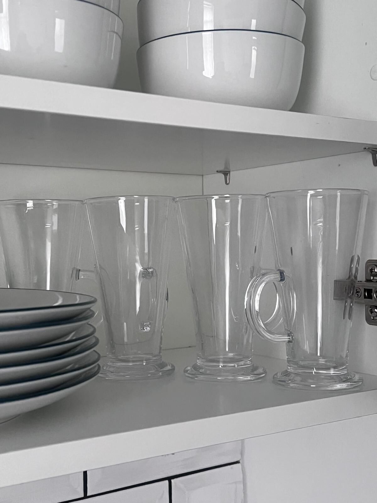 A kitchen shelf with clear glassware and stacked plates.