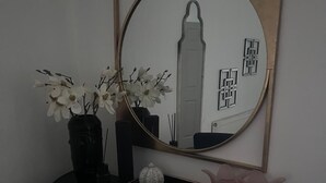 Ein kleiner, dunkelbrauner Tisch mit einem runden Spiegel, einer Vase mit weißen Blumen, einem kleinen weißen Dekoelement und zwei rosa Kerzenhaltern.