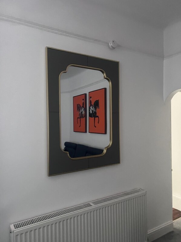 A room with a large mirror on the wall, a radiator below it, and a door leading to another room.