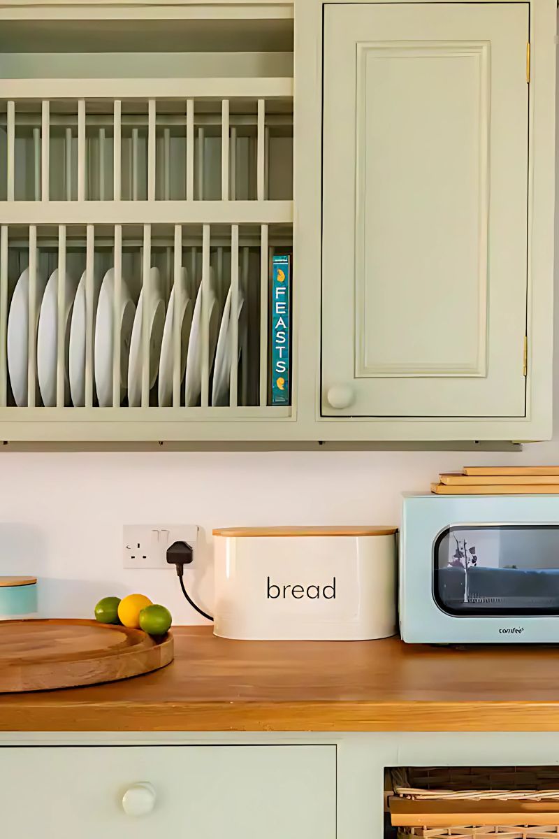 A kitchen with a bread box, a toaster, and a cabinet with dishes.