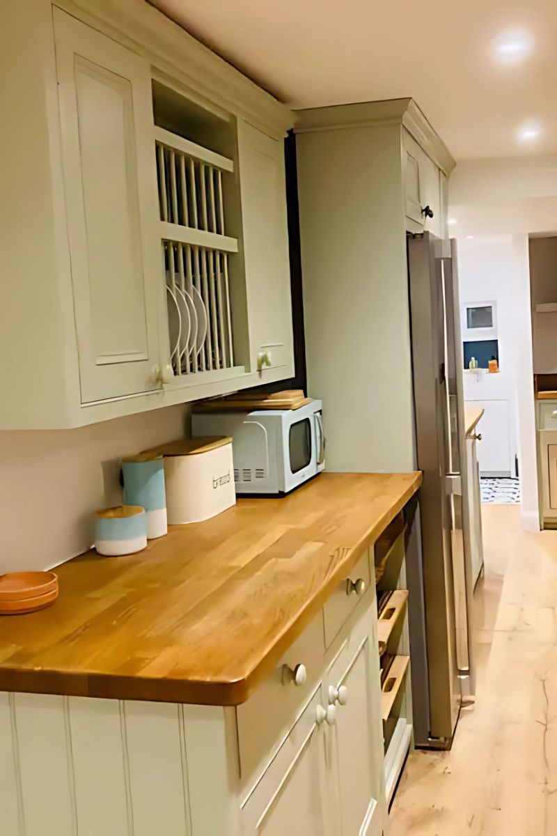 A kitchen with light-colored cabinets, a wooden countertop, a microwave, and a refrigerator.