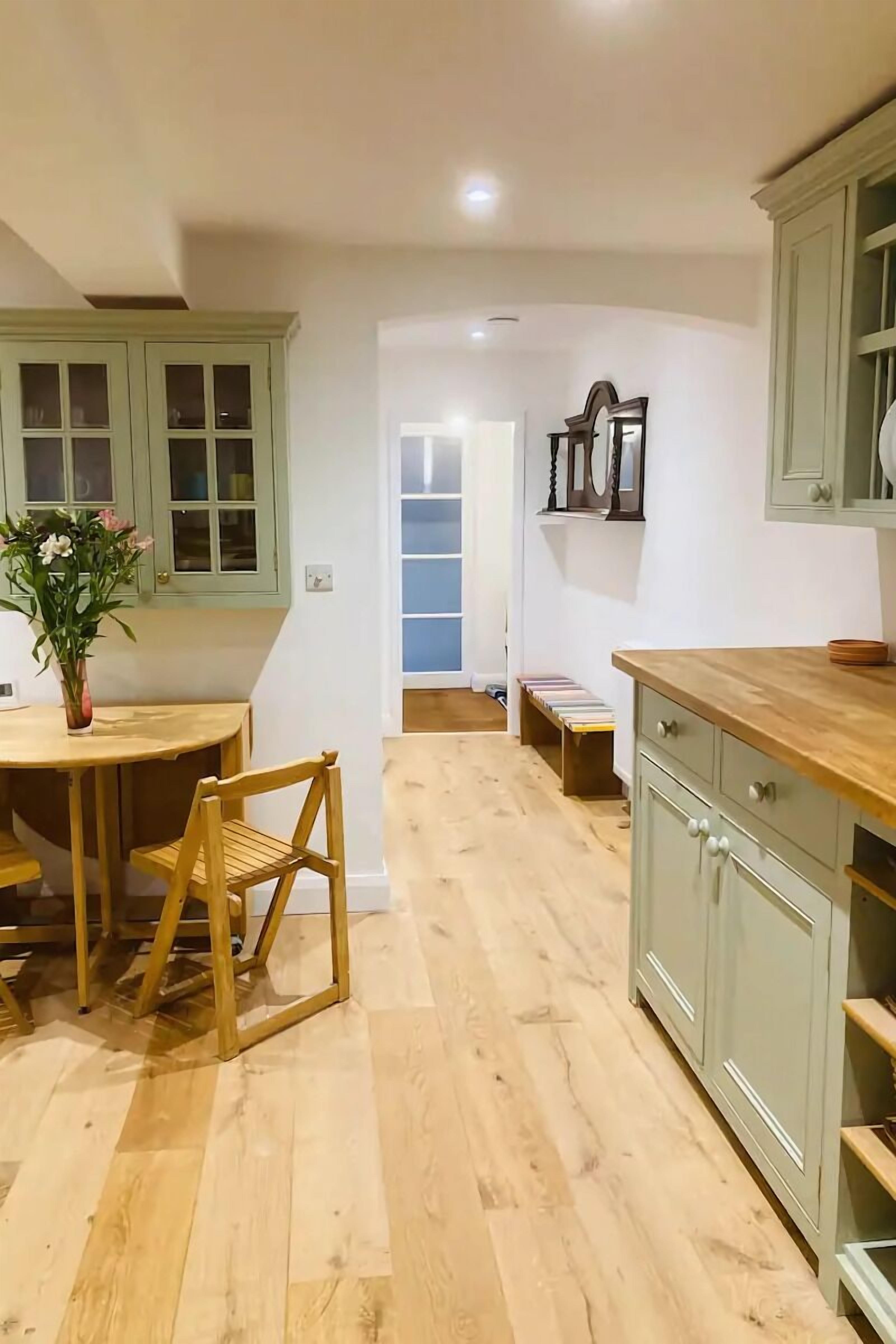 Een keuken met houten vloeren, een eettafel met stoelen en lichtgroene kastjes.