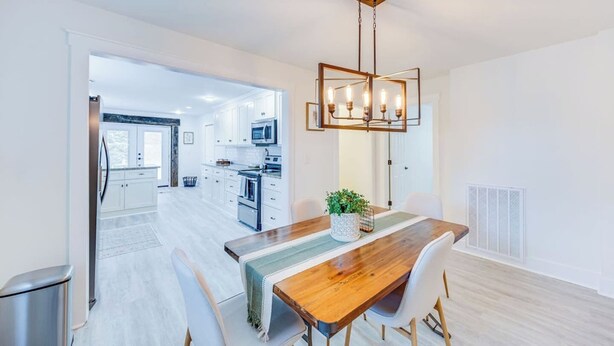 Una cocina moderna con armarios blancos, electrodomésticos de acero inoxidable y una mesa de comedor de madera con sillas.