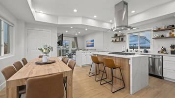 Una cocina moderna con una isla central, armarios blancos y una campana extractora de acero inoxidable.