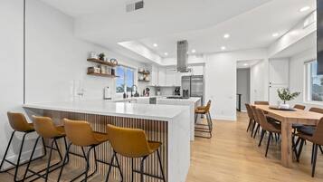 Una cocina moderna con una isla central, taburetes de bar y un comedor con mesas y sillas de madera.