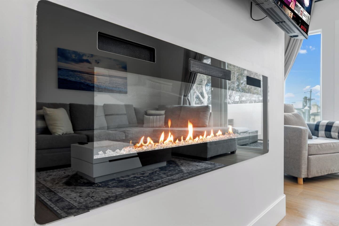 Una sala de estar moderna con chimenea integrada, sofás grises y un ventanal con vistas a la ciudad.