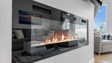 Una sala de estar moderna con chimenea integrada, sofás grises y un ventanal con vistas a la ciudad.