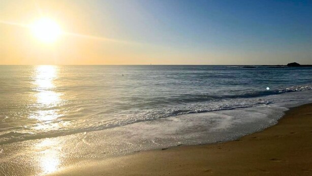 Ein Strand mit blauem Himmel und der Sonne, die sich im Wasser spiegelt.