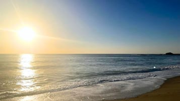 A beach with a clear sky and the sun reflecting on the water.