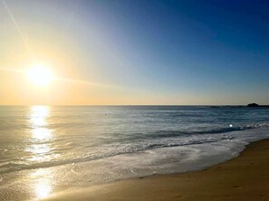 Une plage avec un ciel dégagé et le soleil se reflétant sur l’eau.