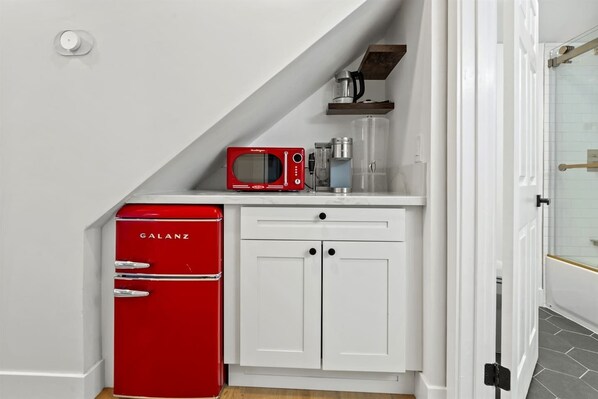 Une cuisine compacte avec un réfrigérateur Galanz rouge, un four à micro-ondes et une machine à café, le tout posé sur un plan de travail blanc.
