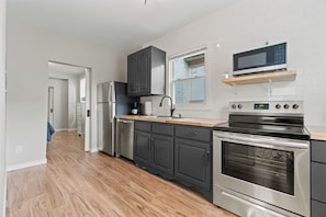 A modern kitchen with dark cabinets, a stainless steel refrigerator, a built-in oven, and a microwave on a shelf.