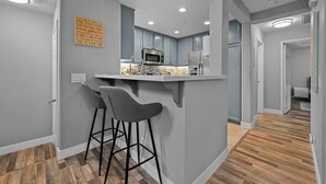 Une cuisine moderne avec des meubles gris, un four à micro-ondes et un coin bar équipé de deux tabourets.