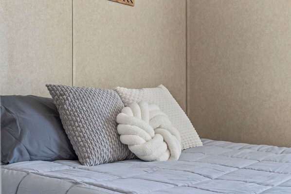 A bed with a grey quilt, a grey pillow, and a white pillow with a leaf pattern.