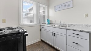 A kitchen with white cabinets, a black stove, a sink, and a window with blinds.