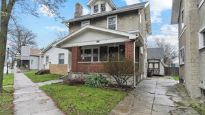 A two-story house with a front porch, a brick chimney, and a small front yard.
