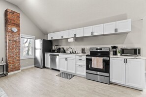 A kitchen with white cabinets, a brick wall, stainless steel appliances, and a window.