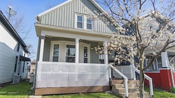 A two-story house with a porch, a small tree with blossoms, and a satellite dish.