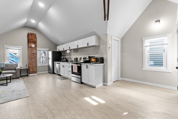 A modern kitchen with white cabinets, a brick accent wall, and a dining area with a gray sofa.