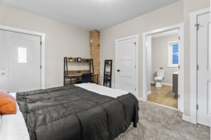 A bedroom with a bed, a desk, a chair, and a bathroom visible through an open door. - Well-Located 2BR Downtown Apartment | Central Stay (Fort Wayne)