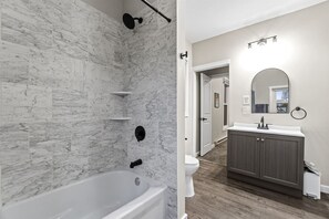 A bathroom with a marble shower wall, a bathtub, a toilet, and a vanity with a mirror. - Well-Located 2BR Downtown Apartment | Central Stay (Fort Wayne)